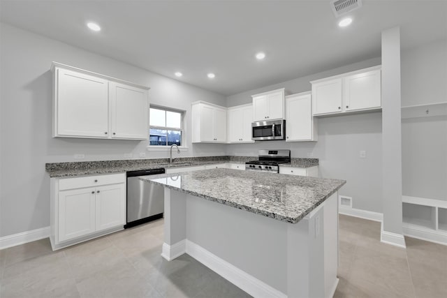 kitchen featuring white cabinetry, sink, light stone countertops, a kitchen island, and appliances with stainless steel finishes