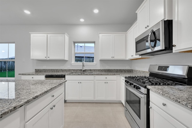 kitchen with light stone countertops, white cabinetry, sink, stainless steel appliances, and light tile patterned floors