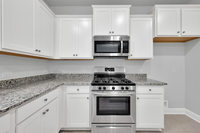 kitchen featuring white cabinets, appliances with stainless steel finishes, light stone counters, and light tile patterned flooring