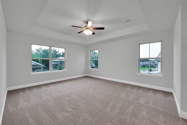 carpeted empty room with ceiling fan, a healthy amount of sunlight, and a tray ceiling