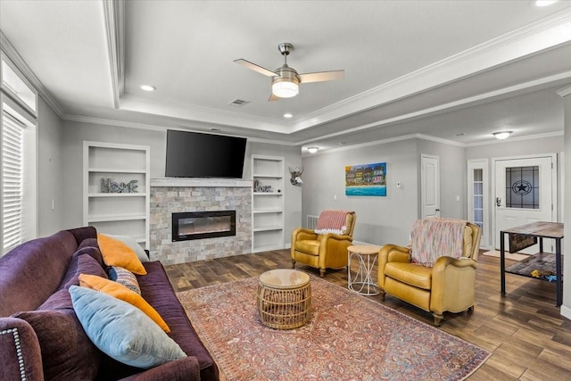 living room featuring ceiling fan, built in features, wood-type flooring, a fireplace, and ornamental molding