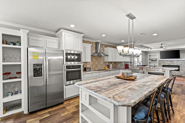 kitchen featuring white cabinetry, stainless steel fridge, decorative light fixtures, and wall chimney range hood