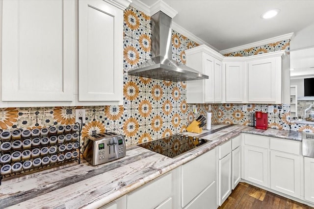 kitchen featuring black electric stovetop, tasteful backsplash, crown molding, wall chimney range hood, and white cabinetry