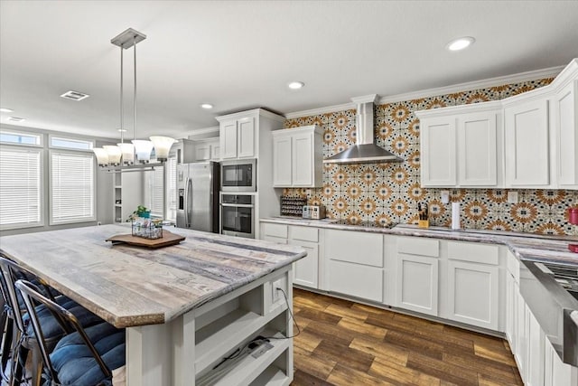 kitchen with white cabinetry, wall chimney range hood, stainless steel appliances, and hanging light fixtures