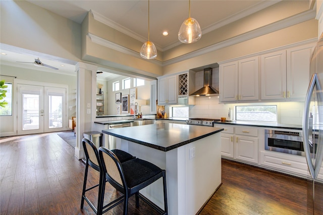 kitchen featuring a kitchen breakfast bar, wall chimney range hood, white cabinets, sink, and ceiling fan