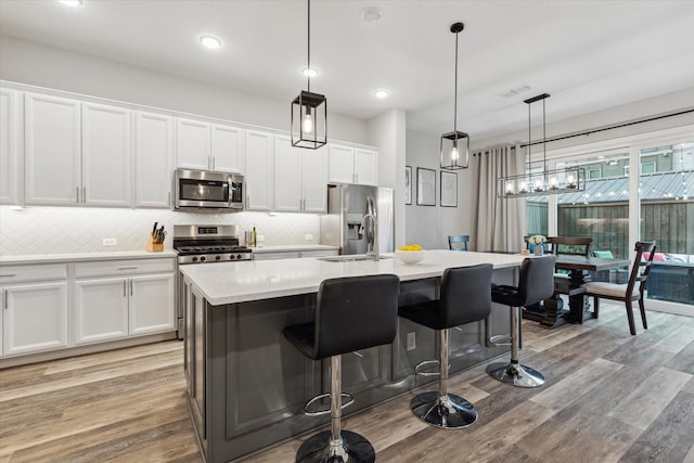 kitchen featuring appliances with stainless steel finishes, a kitchen island with sink, sink, pendant lighting, and white cabinets