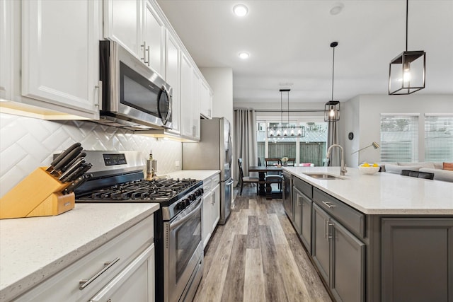 kitchen with sink, white cabinets, stainless steel appliances, and decorative light fixtures