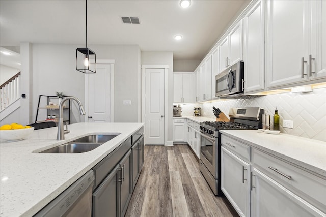 kitchen featuring appliances with stainless steel finishes, light stone counters, sink, white cabinetry, and hanging light fixtures