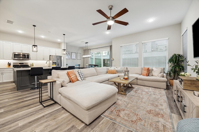 living room with light wood-type flooring, ceiling fan, and sink