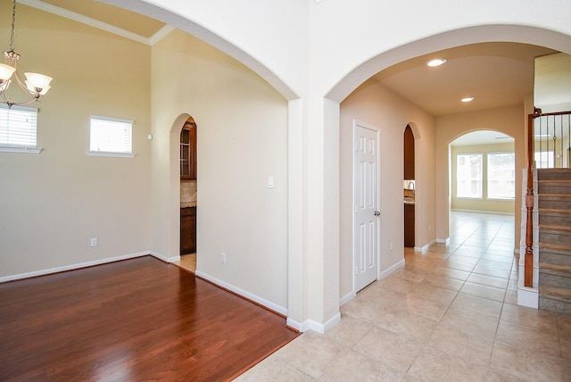 hallway featuring light tile patterned floors, an inviting chandelier, a healthy amount of sunlight, and crown molding