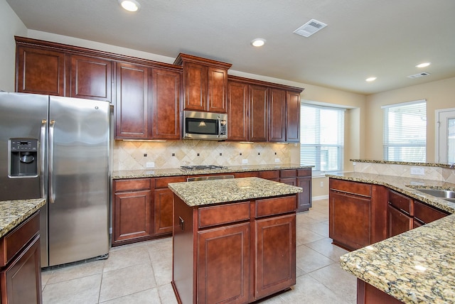 kitchen with light stone countertops, backsplash, stainless steel appliances, sink, and a center island