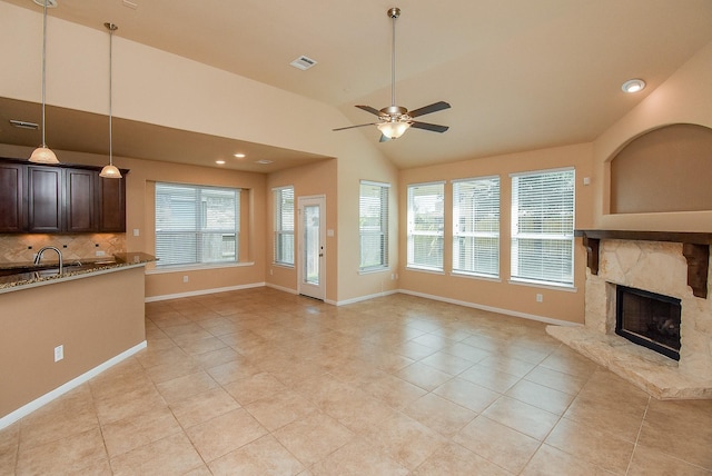 unfurnished living room featuring vaulted ceiling, ceiling fan, sink, a fireplace, and light tile patterned flooring