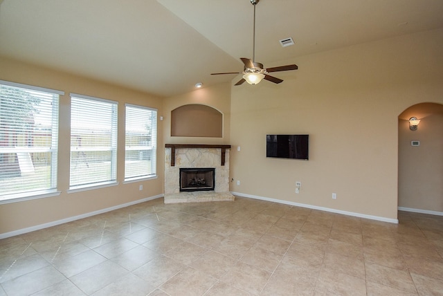 unfurnished living room with ceiling fan, light tile patterned flooring, a stone fireplace, and vaulted ceiling