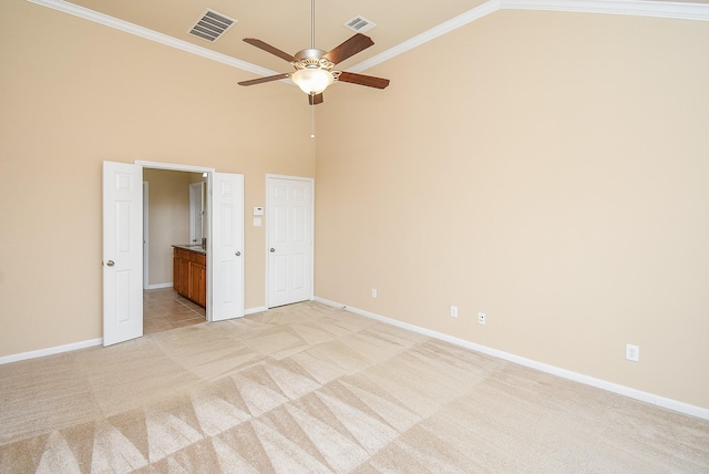 unfurnished bedroom featuring light carpet, a towering ceiling, ensuite bath, ceiling fan, and crown molding