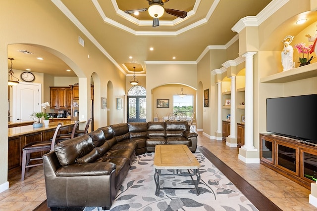 living room with a towering ceiling, ornate columns, ornamental molding, ceiling fan, and built in features