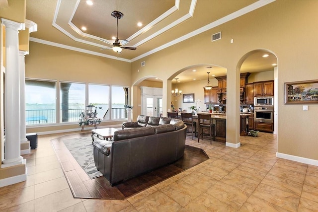 tiled living room with a high ceiling, french doors, ceiling fan with notable chandelier, a raised ceiling, and ornamental molding