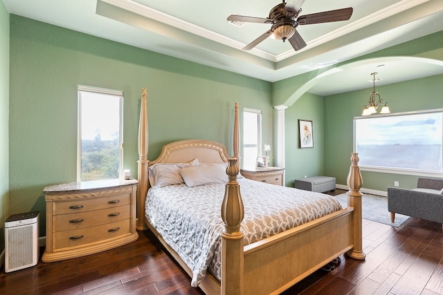 bedroom with a tray ceiling, ornate columns, multiple windows, and ceiling fan with notable chandelier