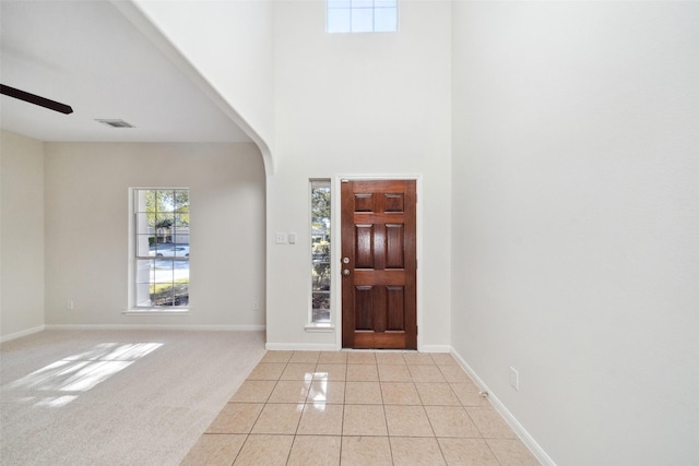 entryway featuring ceiling fan, light colored carpet, and a towering ceiling