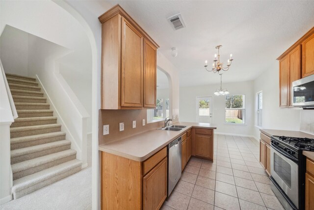 kitchen with sink, an inviting chandelier, kitchen peninsula, pendant lighting, and appliances with stainless steel finishes