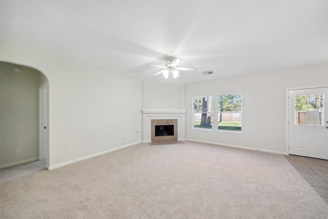 unfurnished living room featuring a tile fireplace, light carpet, and ceiling fan