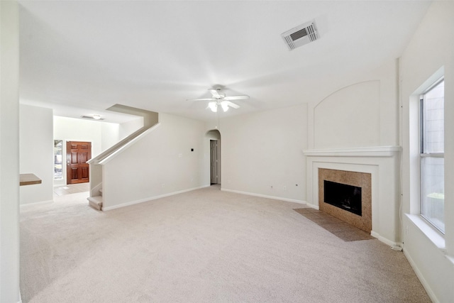 unfurnished living room featuring a tile fireplace, ceiling fan, and light carpet