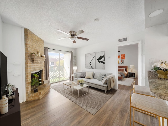 living room featuring ceiling fan, a fireplace, dark wood-type flooring, and a textured ceiling