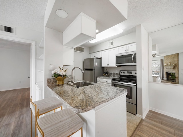 kitchen featuring sink, stainless steel appliances, kitchen peninsula, stone countertops, and a kitchen bar