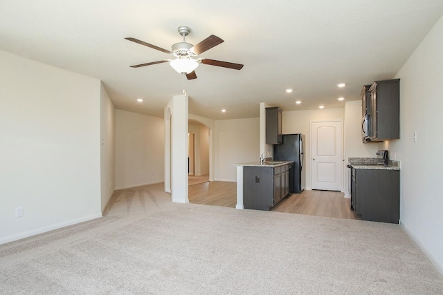 kitchen with ceiling fan, light stone counters, stainless steel appliances, and light carpet