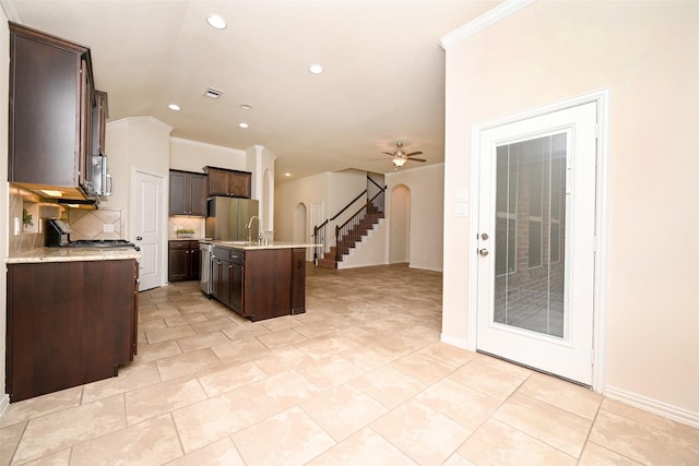 kitchen with ceiling fan, crown molding, an island with sink, dark brown cabinets, and appliances with stainless steel finishes