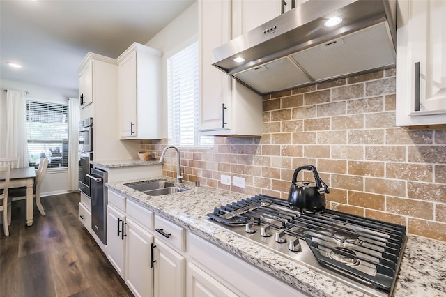 kitchen with light stone countertops, appliances with stainless steel finishes, extractor fan, sink, and white cabinetry