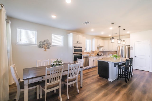 kitchen with light stone countertops, appliances with stainless steel finishes, pendant lighting, white cabinets, and a center island