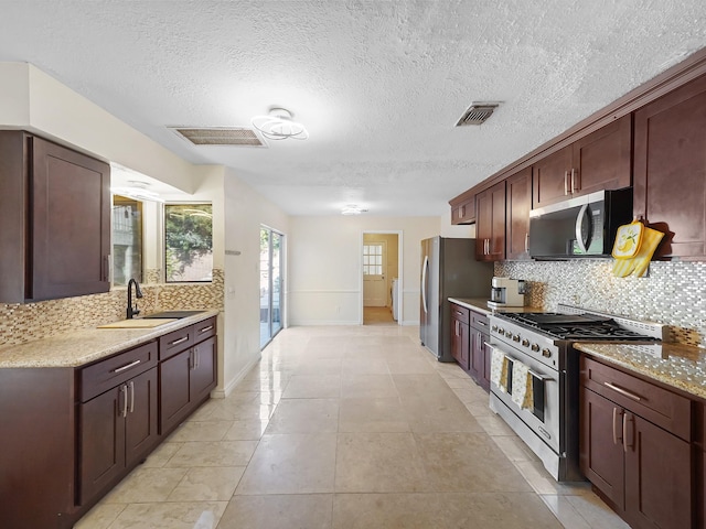 kitchen featuring light stone countertops, appliances with stainless steel finishes, backsplash, sink, and light tile patterned flooring