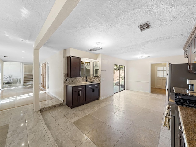 kitchen with decorative backsplash, a textured ceiling, high end stove, dark brown cabinetry, and sink