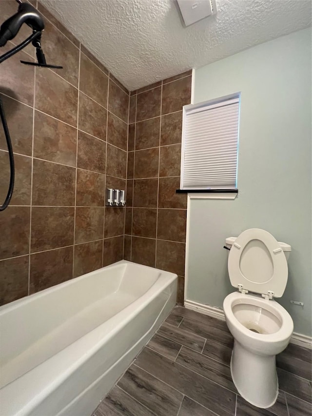 bathroom featuring a textured ceiling, toilet, and tiled shower / bath