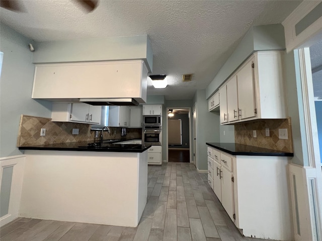 kitchen featuring tasteful backsplash, white cabinetry, stainless steel appliances, and a textured ceiling