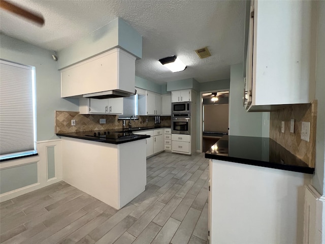 kitchen with kitchen peninsula, a textured ceiling, stainless steel appliances, ceiling fan, and white cabinetry