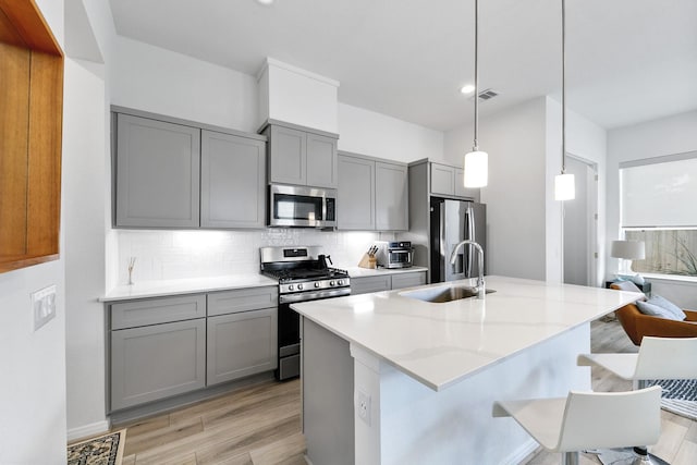 kitchen with light stone countertops, stainless steel appliances, sink, decorative light fixtures, and gray cabinets