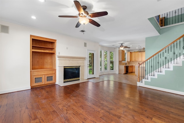 unfurnished living room featuring crown molding, a high end fireplace, wood-type flooring, and ceiling fan