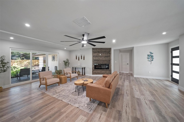 living room featuring a stone fireplace, ceiling fan, and light hardwood / wood-style flooring