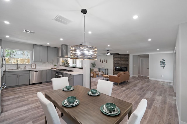 dining space featuring ceiling fan, a large fireplace, light hardwood / wood-style floors, and sink