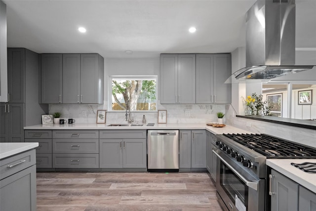 kitchen with sink, gray cabinets, stainless steel appliances, island range hood, and light wood-type flooring