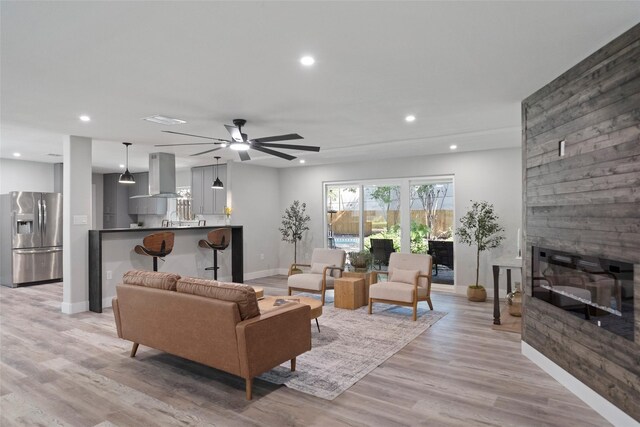 living room with a large fireplace, light hardwood / wood-style flooring, and ceiling fan