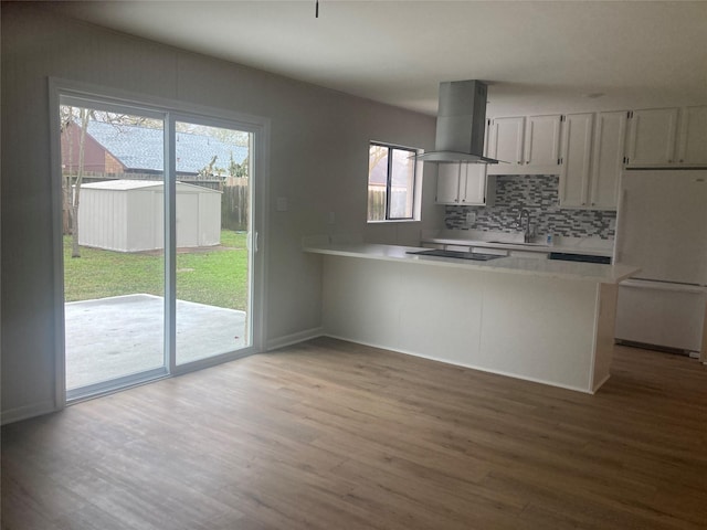 kitchen with kitchen peninsula, tasteful backsplash, ventilation hood, white refrigerator, and light hardwood / wood-style flooring