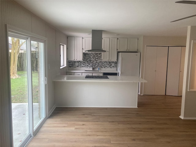 kitchen featuring white cabinets, white fridge, kitchen peninsula, and wall chimney range hood