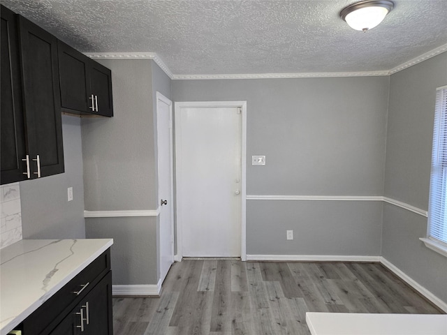 kitchen with a textured ceiling, light hardwood / wood-style floors, light stone countertops, and crown molding