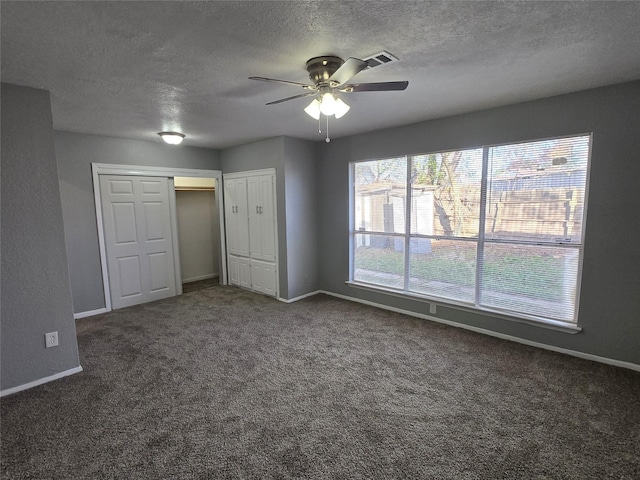 unfurnished bedroom with ceiling fan, dark carpet, and a textured ceiling