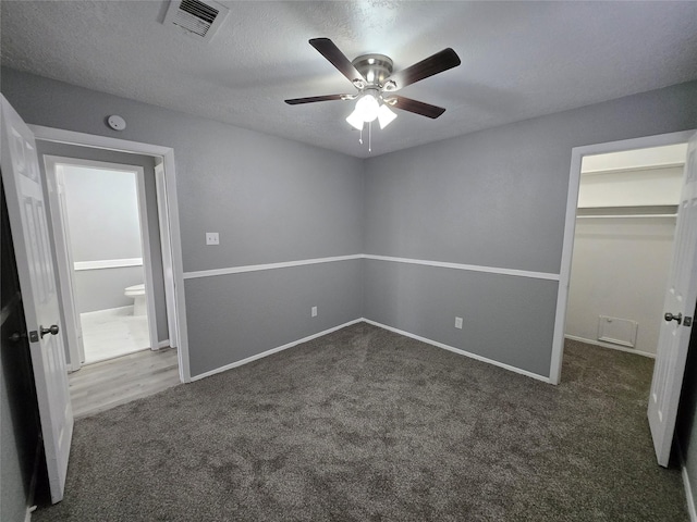 unfurnished bedroom with dark colored carpet, a walk in closet, ceiling fan, a textured ceiling, and a closet