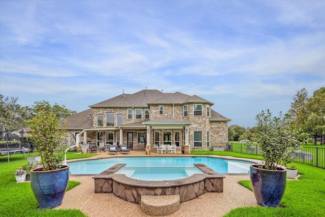 back of property with a fenced in pool, a lawn, and a trampoline