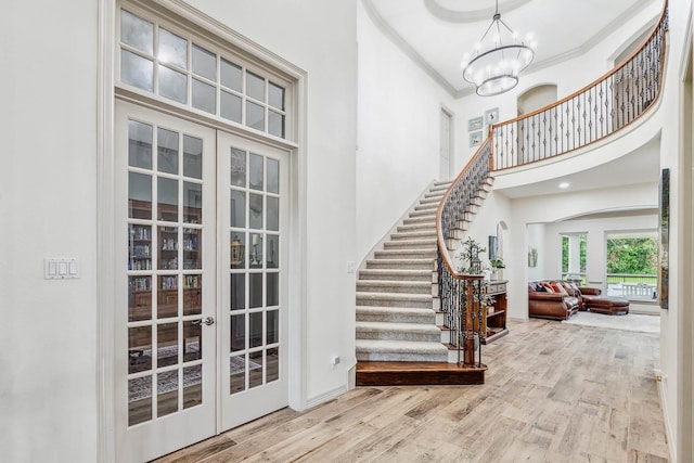 foyer with french doors, crown molding, hardwood / wood-style flooring, a notable chandelier, and a high ceiling