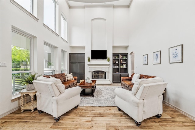 living room with a towering ceiling, light hardwood / wood-style flooring, and crown molding